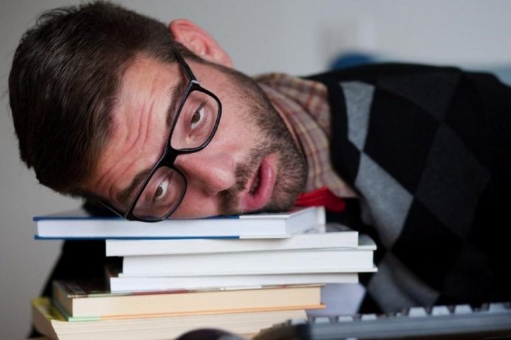 مرد عینکی دچار کمبود خواب روی چند کتاب و دفتر