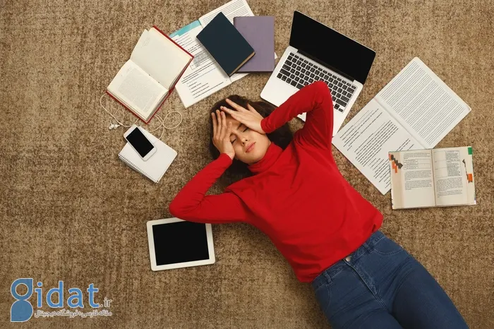 سردرد دختر لباس قرمز روی زمین کنار کتاب و لپتاپ