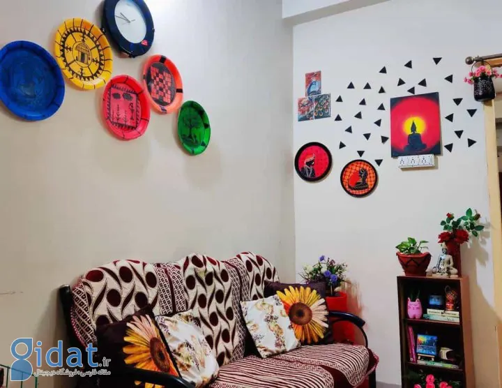 خانه‌ای با دکوراسیون الهام‌بخش: تابلوهای رنگی روی دیوار، مبل با کوسن‌های طرح گل و یک قفسه کوچک کتاب